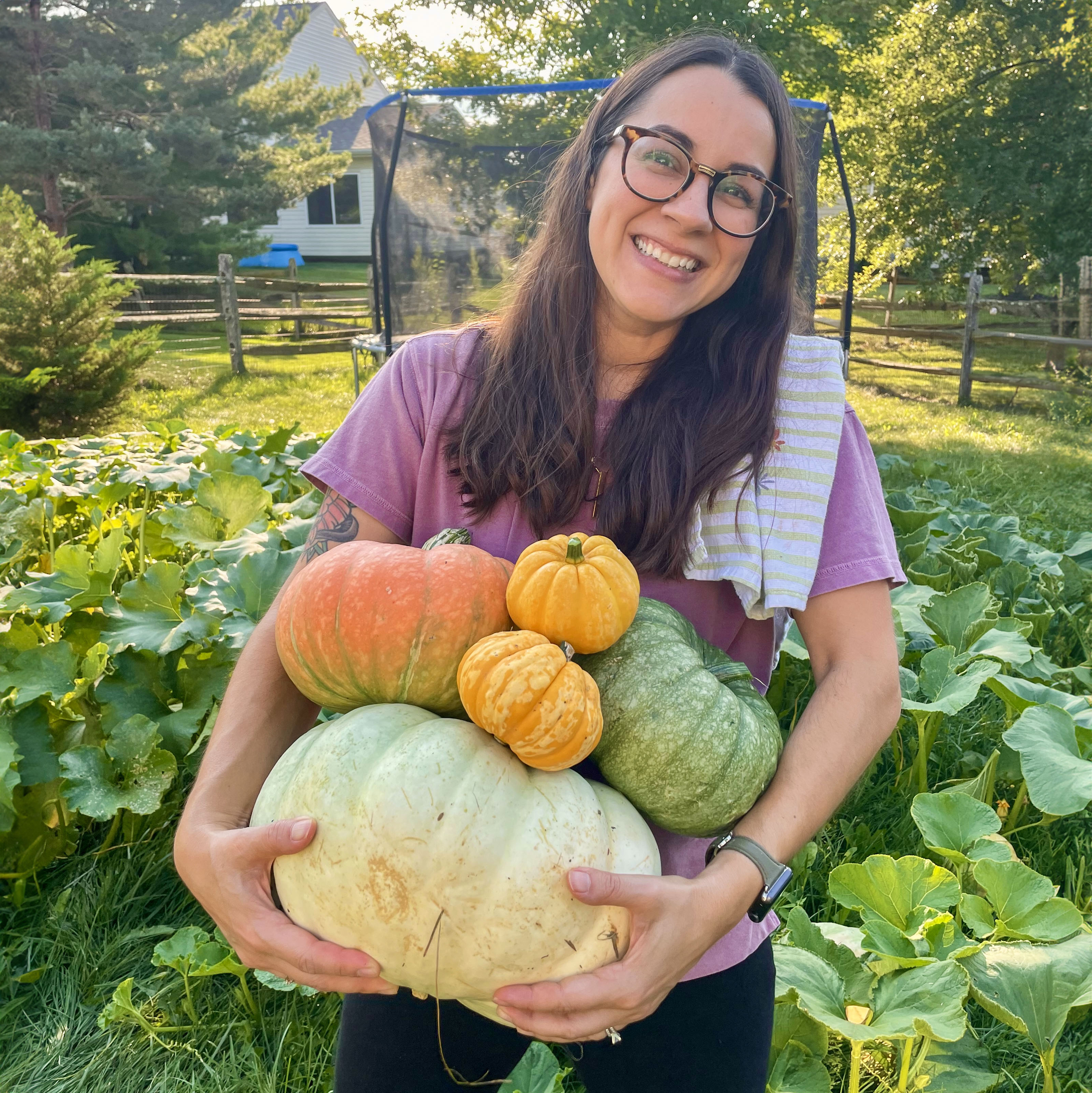 Rhea holds multiple homegrown heirloom pumpkins of various colors and textures.
